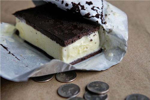 An ice cream sandwich, partially unwrapped atop a pile of quarters.