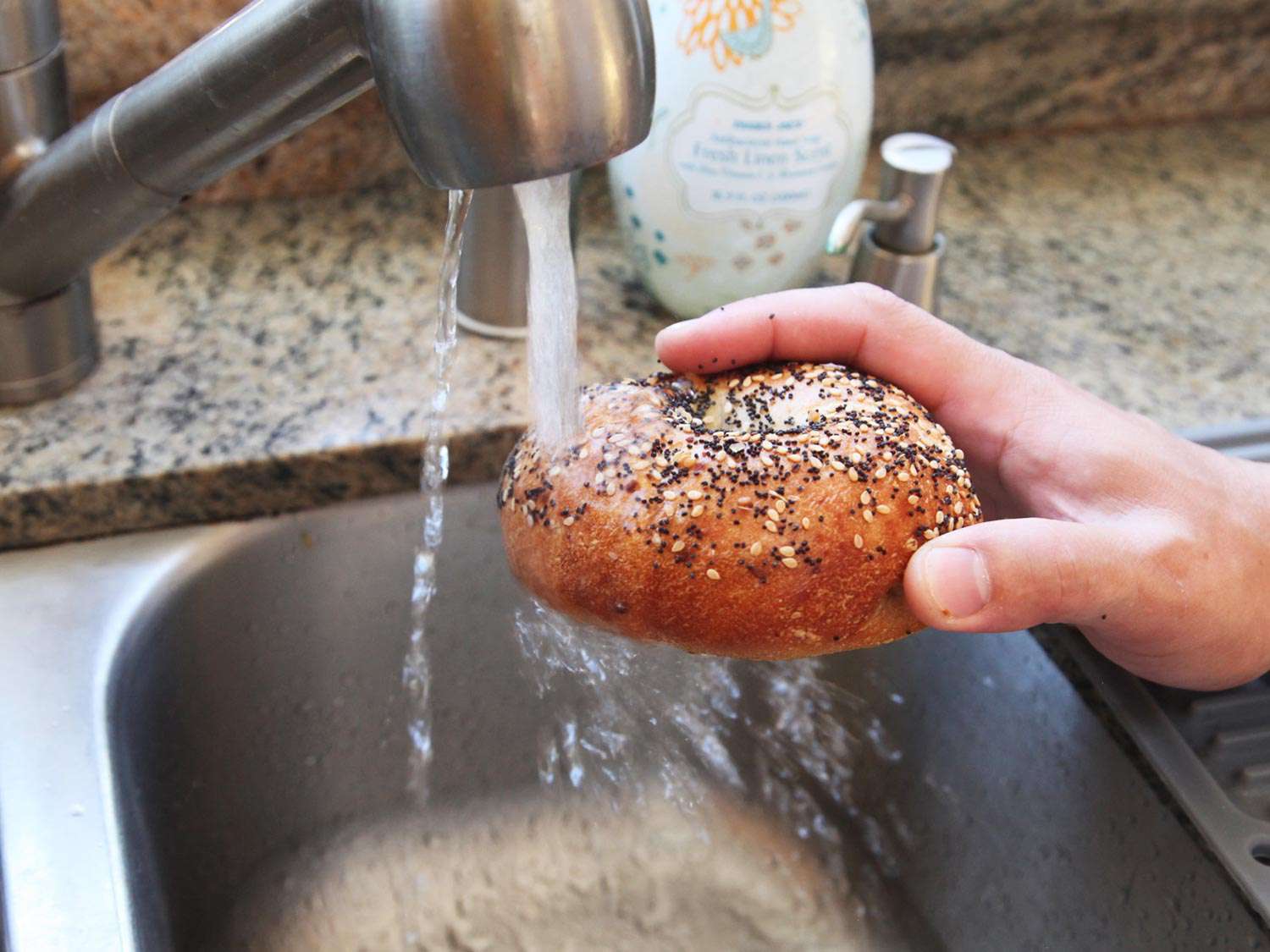 A bagel being placed under a faucet with the water turned on. 
