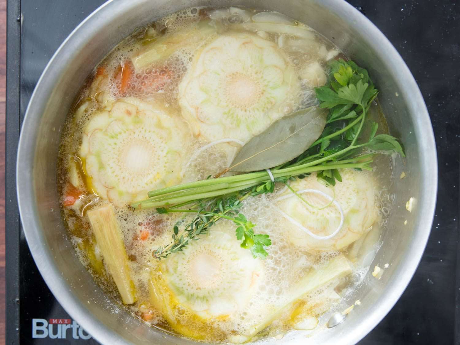 Overhead view of the saucier pan filled with aromatics, artichokes, and stock.