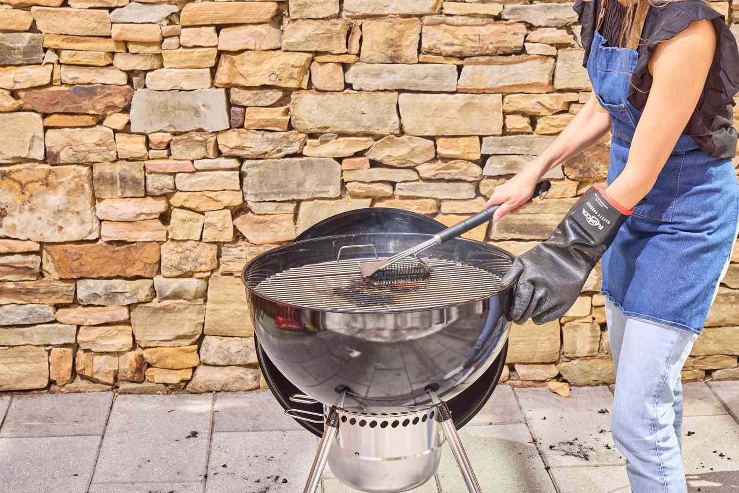 A person using a brush to clean the Weber Original Kettle Premium 22-Inch Charcoal Grill