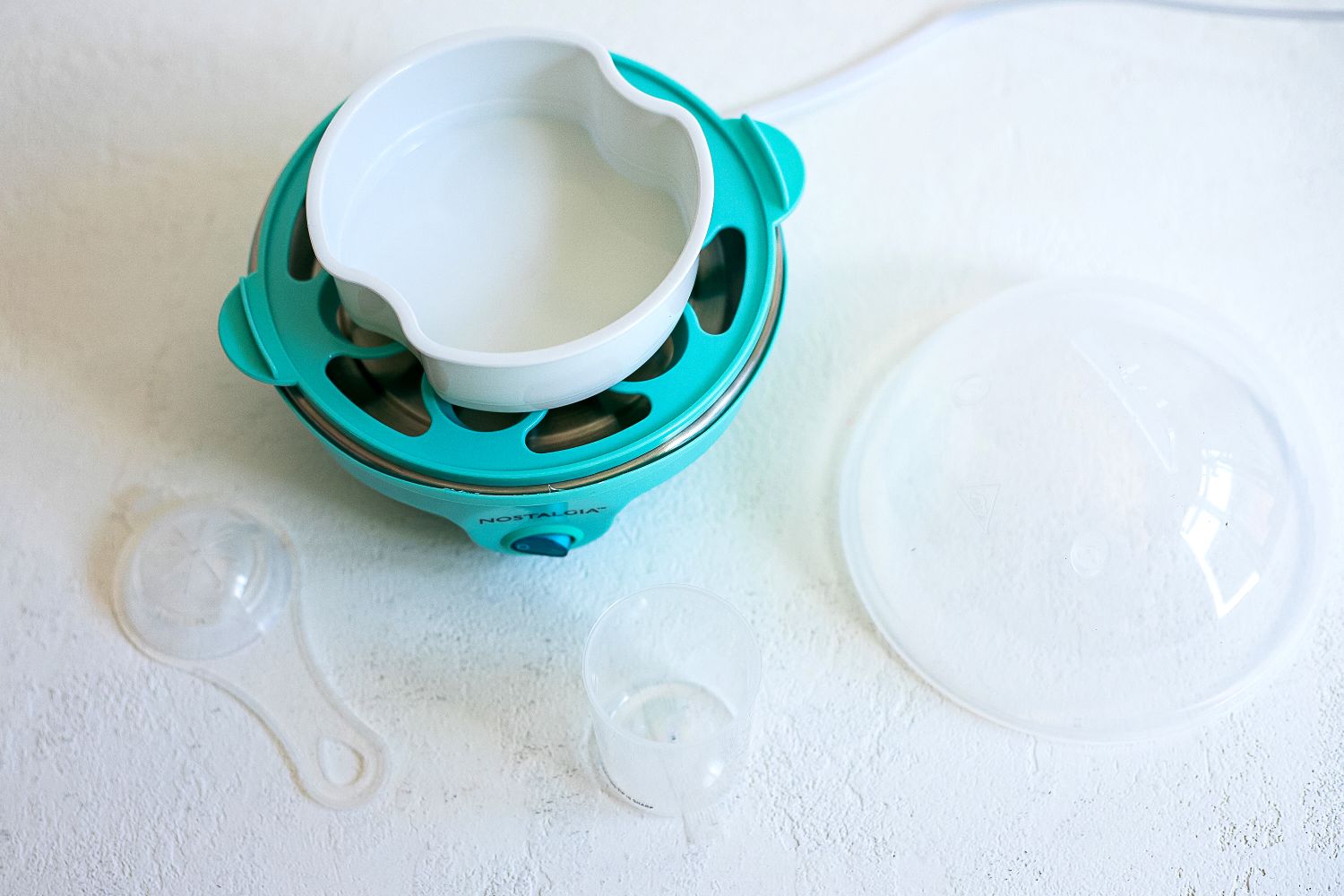 All of the parts of an egg cooker sitting on a white surface