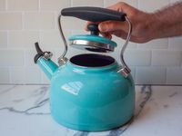 a person removing the lid on a blue kettle
