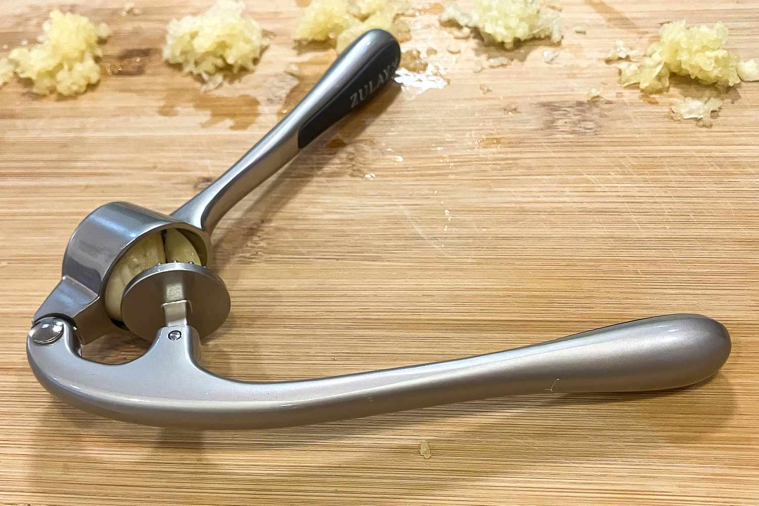 A garlic press with crushed garlic on a cutting board