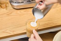 A person pours frothed milk into espresso made in the Breville The Oracle Jet Espresso Machine