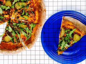 Slice of cheeseburger pizza on a blue plate. Rest of cheeseburger pizza on graphic background 