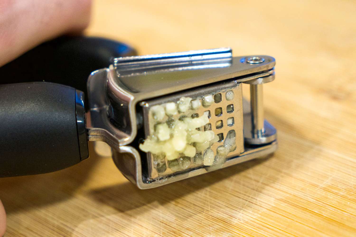 A garlic press with freshly minced garlic extruded through the holes