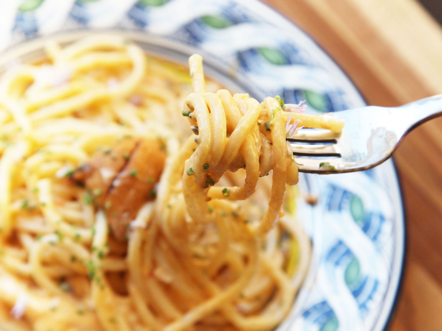 Close-up of a forkful of sea urchin bucatini garnished with minced chives, chive flowers, and fresh sea urchin tongues.