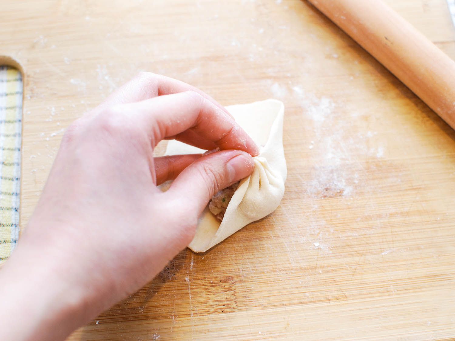 Gathering and pinching the pleats of a sheng jian bao wrapper together.