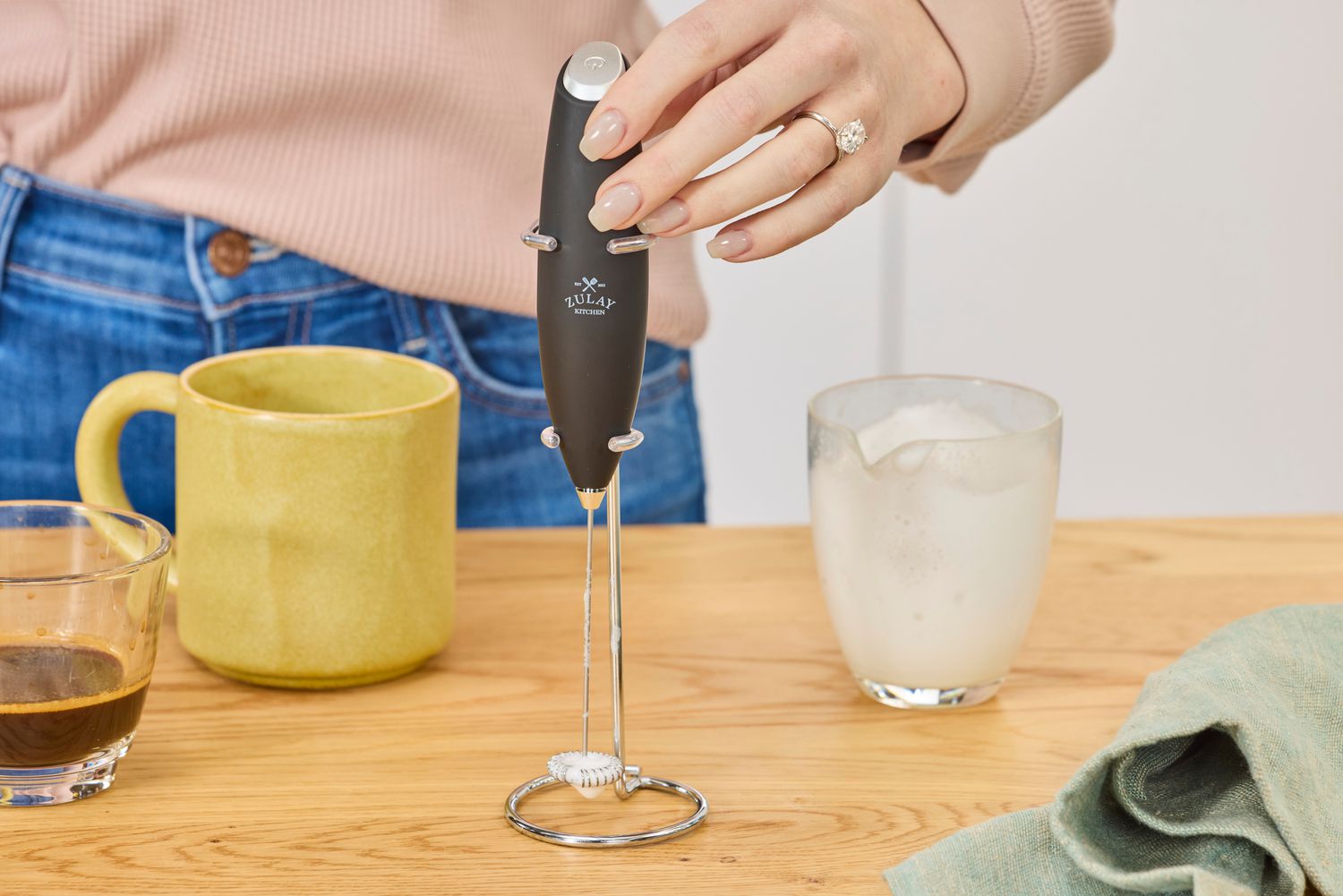 A person removing the Zulay milk frother from its stand.