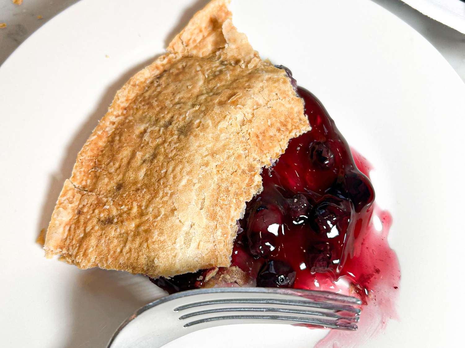 Slice of berry pie on a white plate with a fork