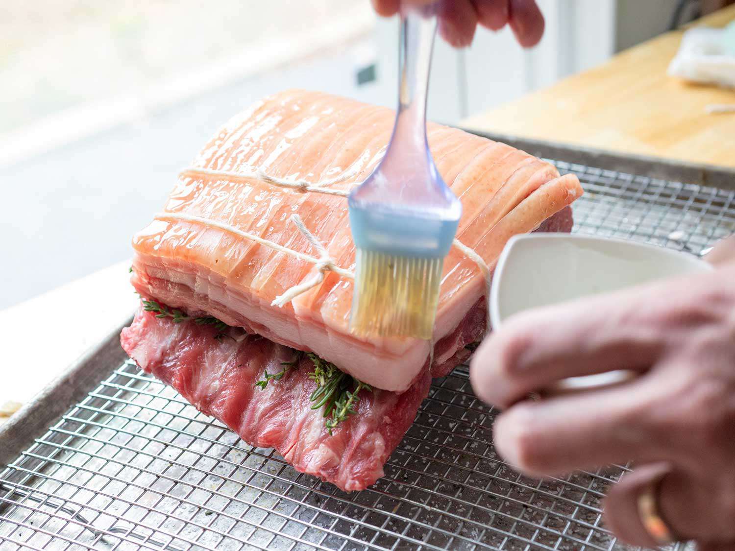 Brushing oil over a raw pork loin roast that's been bound with twine