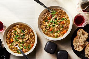 2 bowls Chicken Lentil stew with a plates of sliced bread on the side, black salt and pepper shakers, and a glass and bottle of red wine 
