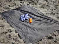 the matador picnic blanket on the beach with a pair of sandals and a bottle of sunscreen on it