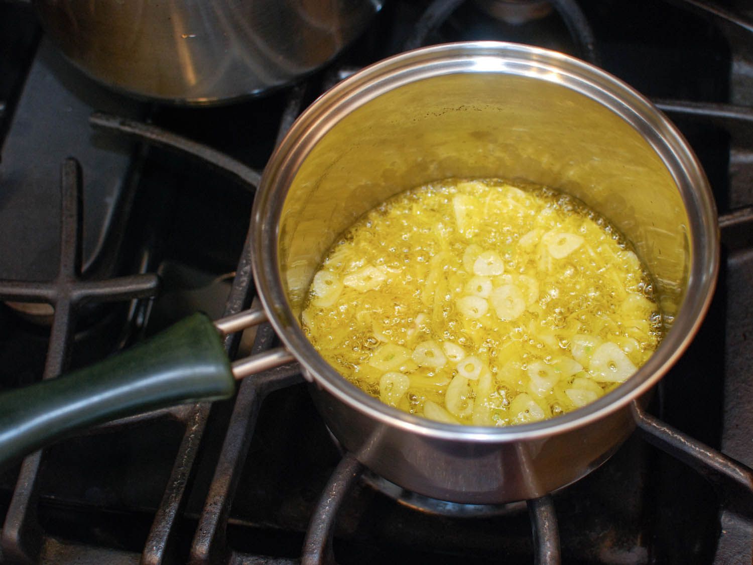 Garlic slices are fried in oil in a small saucepan.