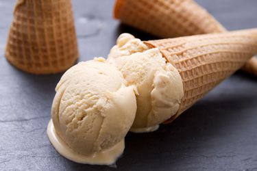 A double scoop of sugar cone ice cream in a sugar cone, arranged on its side on a black slate surface.