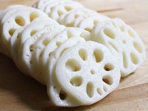 Slices of lotus root shingled on a wooden cutting board.