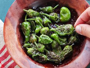 A small wooden bowl of grilled Padrón peppers sprinkled with salt. 