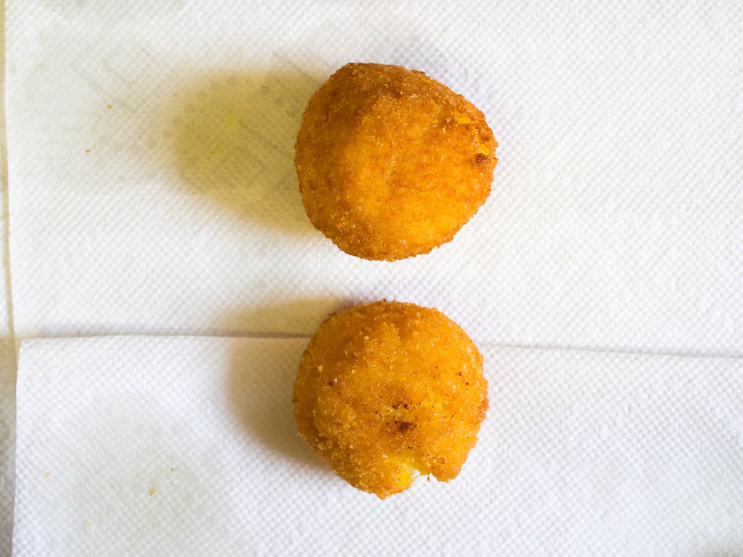 Overhead close-up of two arancini draining on a layer of paper towel.