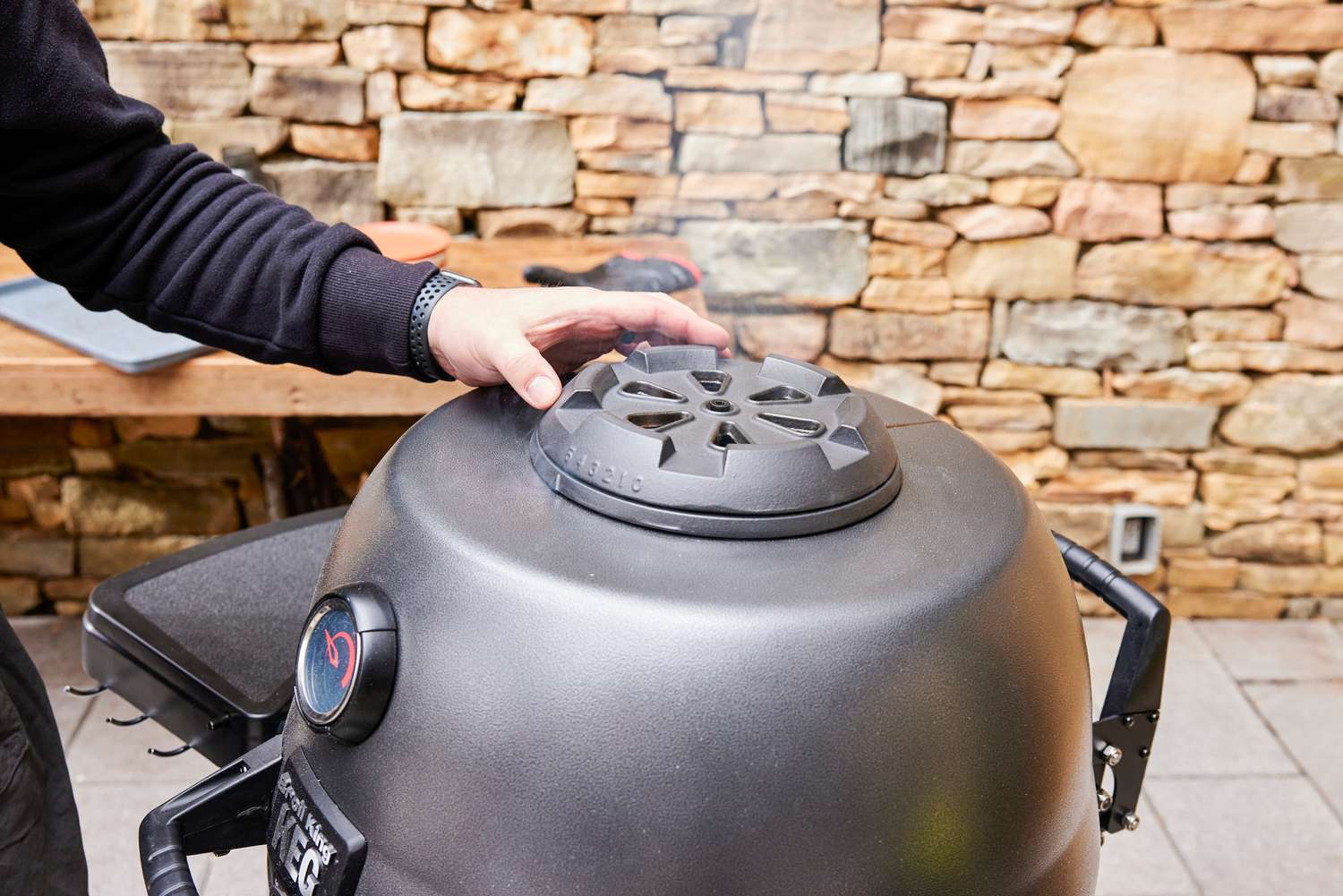A person opens the vent on the top of the Broil King Keg Kamado Charcoal Grill