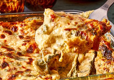 A serving of lasagna being lifted from a glass baking dish with melted cheese and visible layers