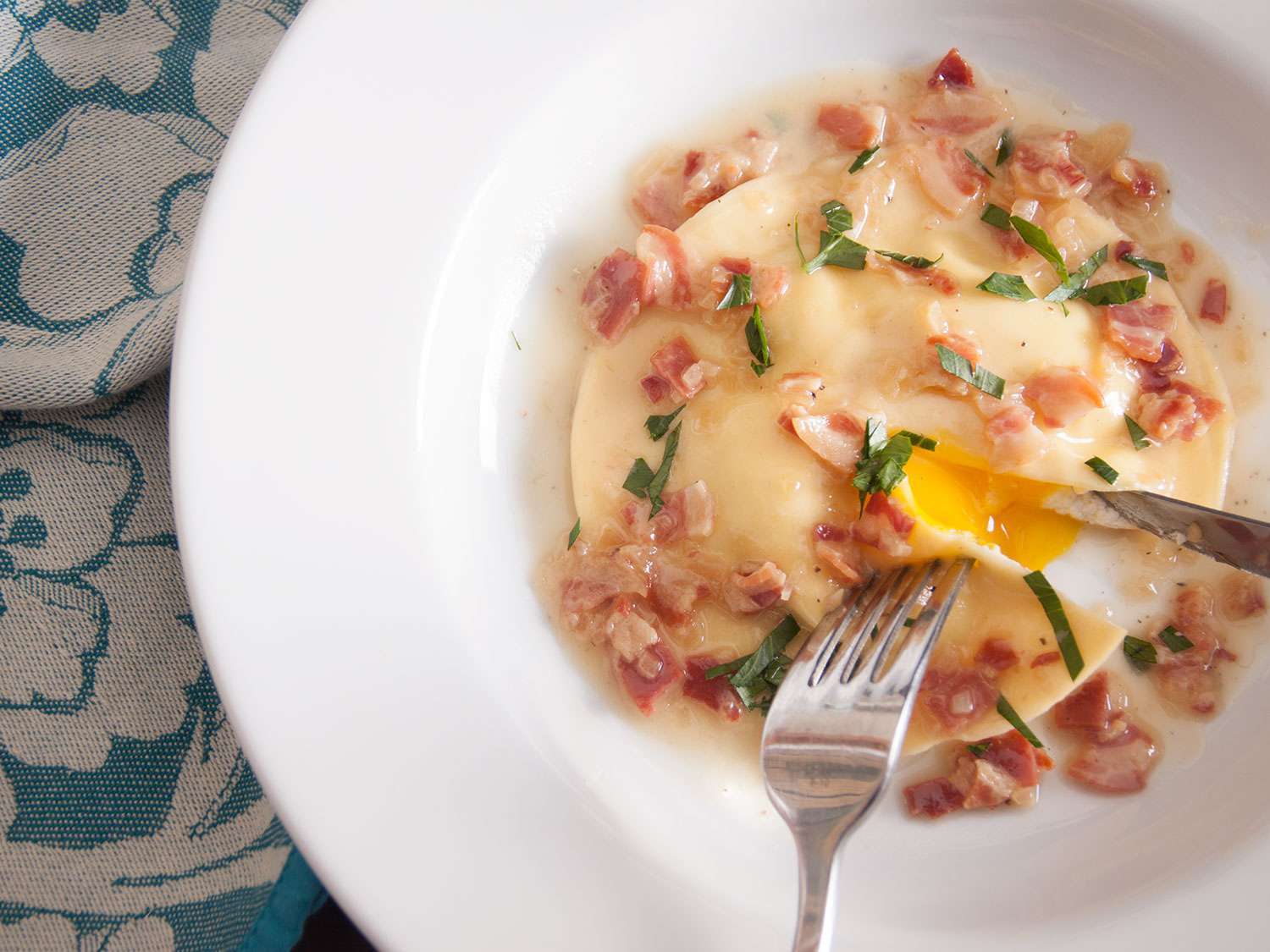 Overhead closeup of a runny egg yolk raviolo, served in a white bowl.