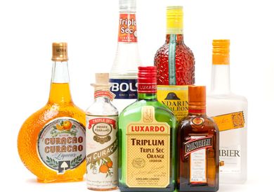 Seven different brands and styles of orange liqueur on a white surface