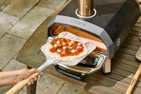 A person places a pizza into the Ooni Karu 2 Multi-Fuel Pizza Oven