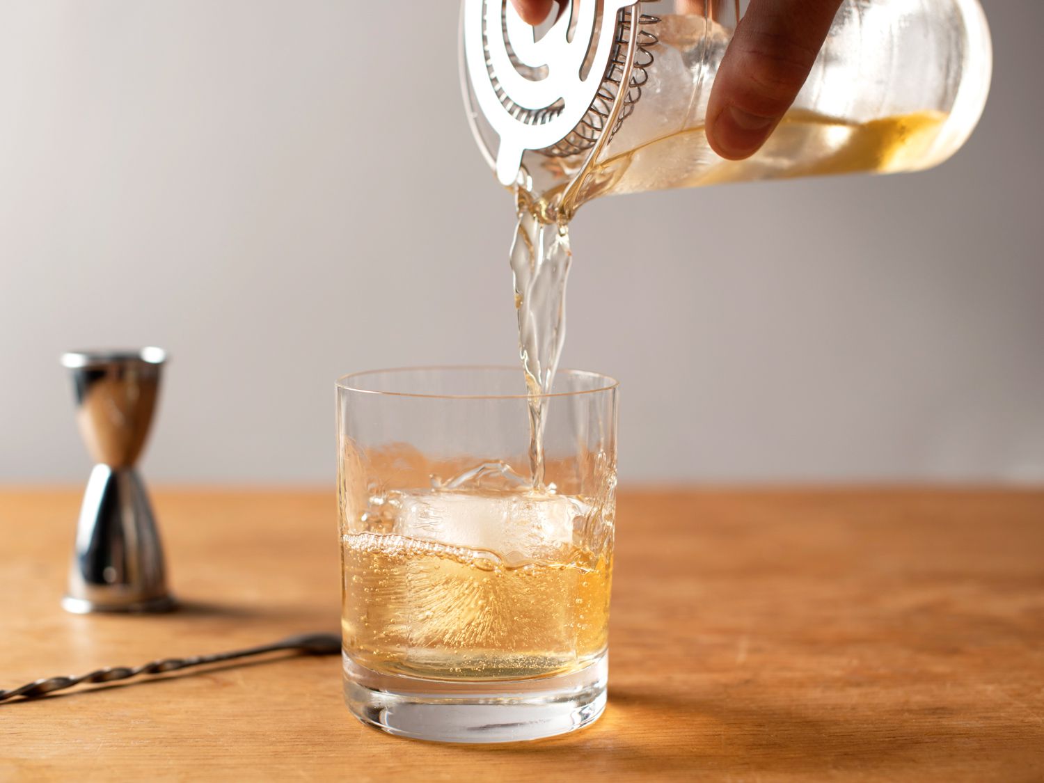 straining a Godfather cocktail into a rocks glass with ice 