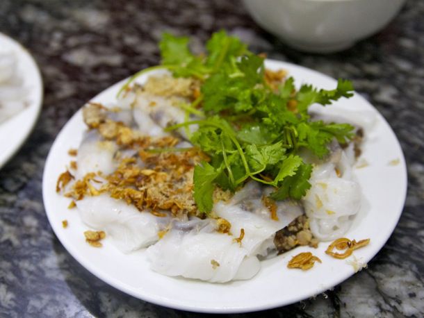 Bánh cuốn resting on a white plate with leafy greens on top 
