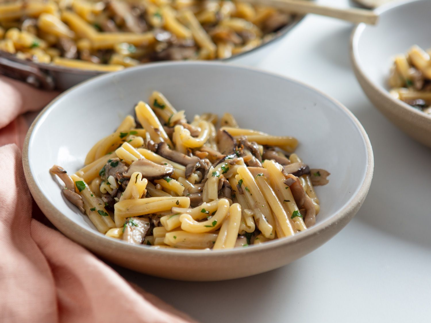 Two servings of pasta ai funghi in ceramic bowls next to the cooking skillet.