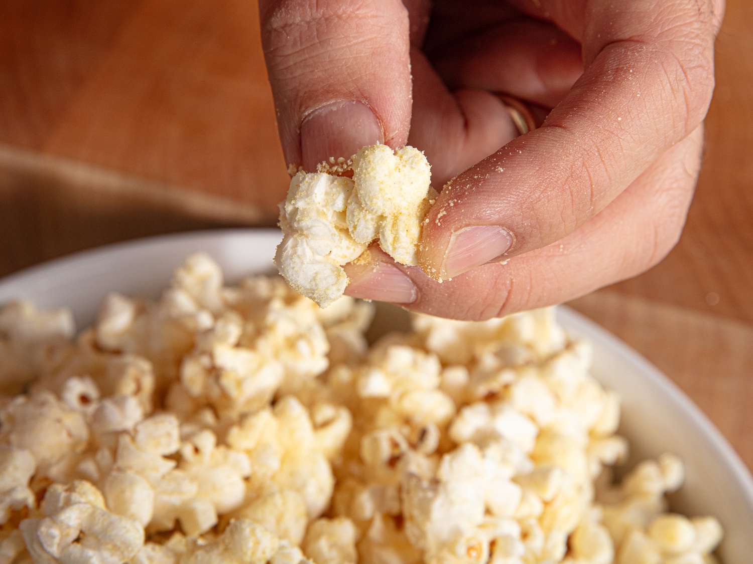 A hand lifting a piece of honey mustard popcorn