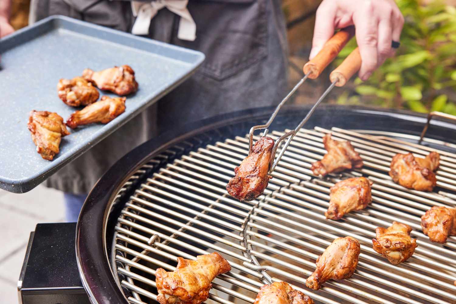A person cooks chicken in the Weber 18201001 Summit Kamado E6 Charcoal Grill