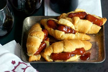 Four glazed cocktail sausage and crescent roll sandwiches, served on a small baking sheet.