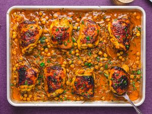 Baked chicken thighs with chickpeas on a tray garnished with herbs in a savory sauce