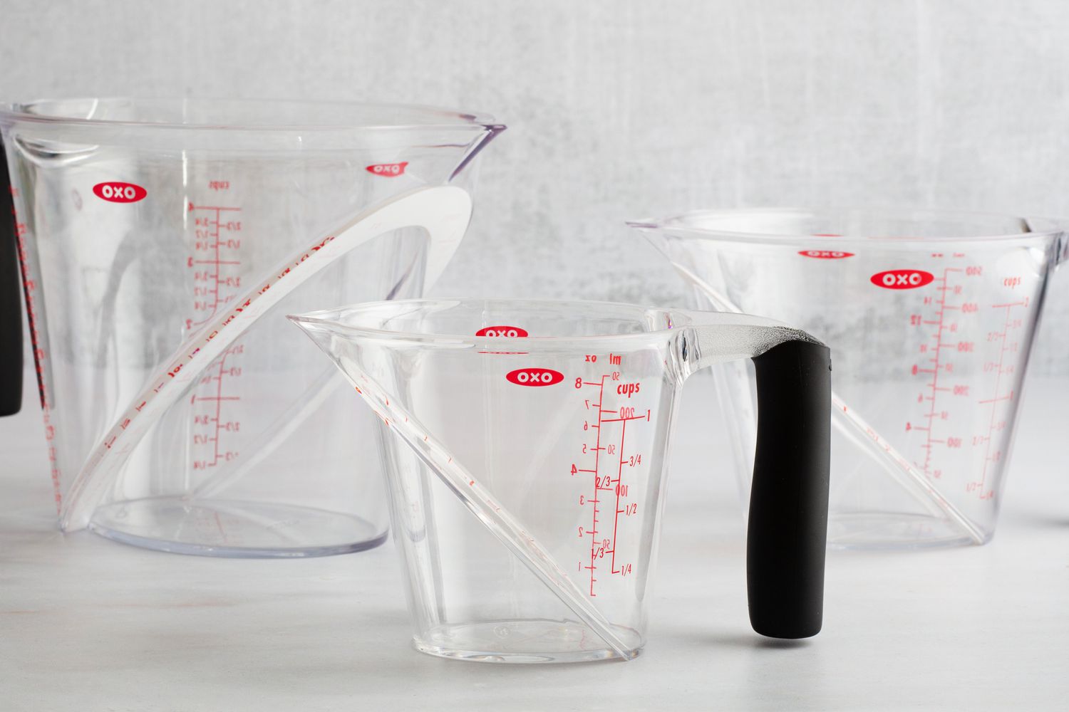 Three plastic OXO liquid measuring cups on a marble surface.