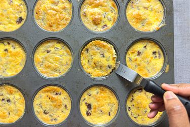 Muffin tin with cooked bacon and egg bites, hand using knife to remove one