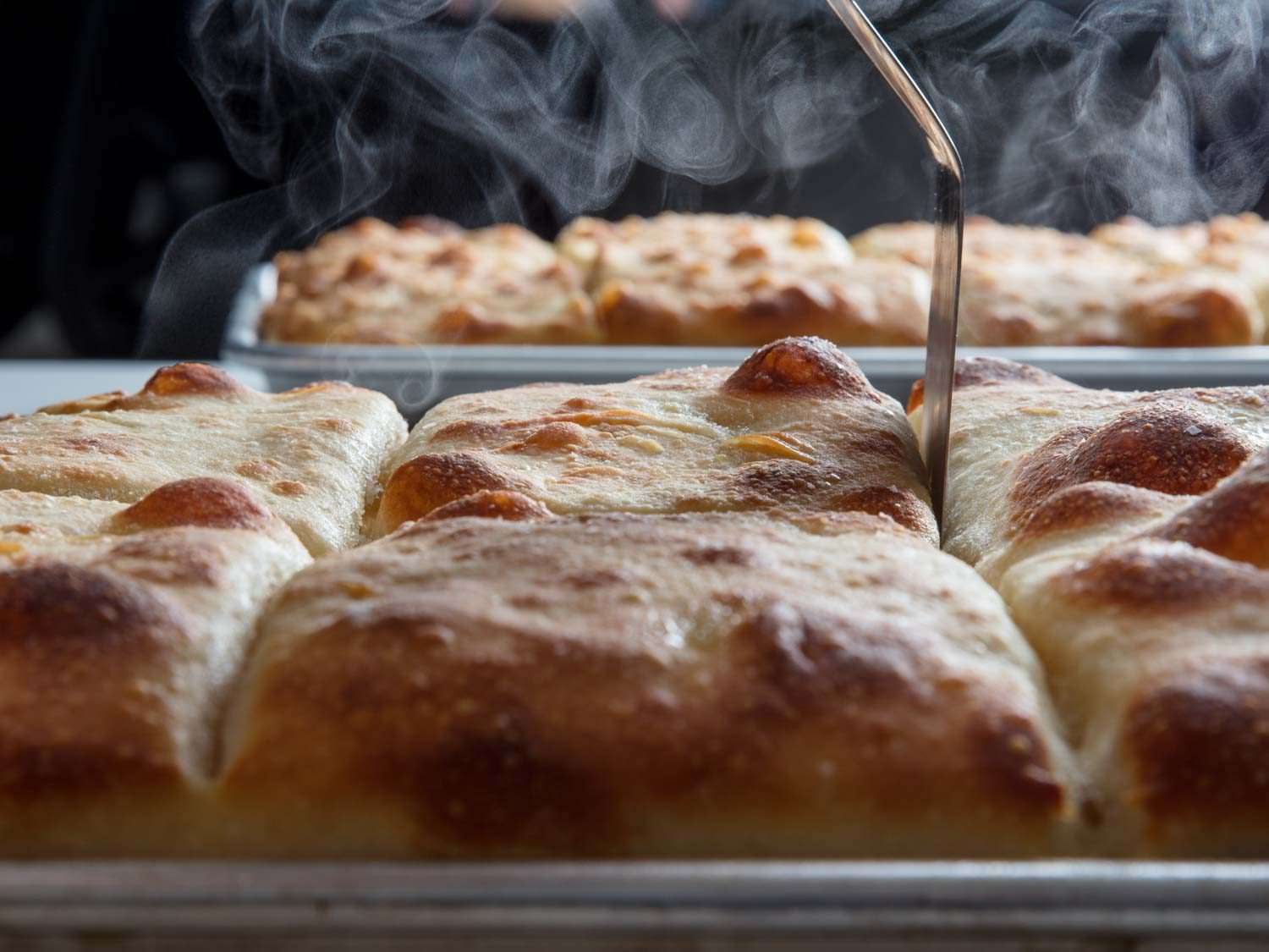 Closeup of spatula dividing steaming portions of trapizzino.