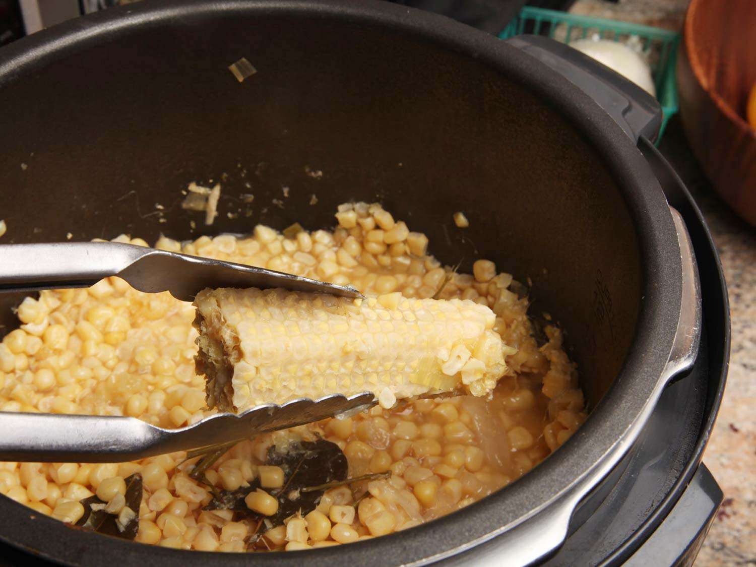 Removing a shaved corn cob from the pressure cooker with tongs.