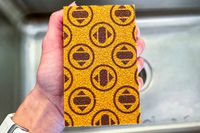 An orange Skura dishwashing sponge being held over a kitchen sink