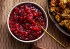 Finished cranberry sauce in a small bowl next to a bowl of stuffing with a gold spoon