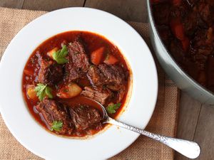 A white serving bowl of goulash sits next to a Dutch oven.