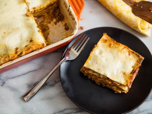 A slice of lasagna Bolognese served from a baking dish on a black plate.