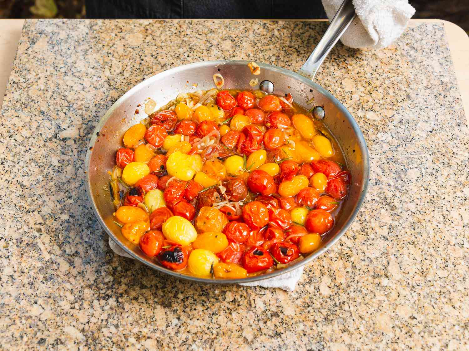 Burst cherry tomatoes and aromatics in pan after cooking in outdoor pizza oven