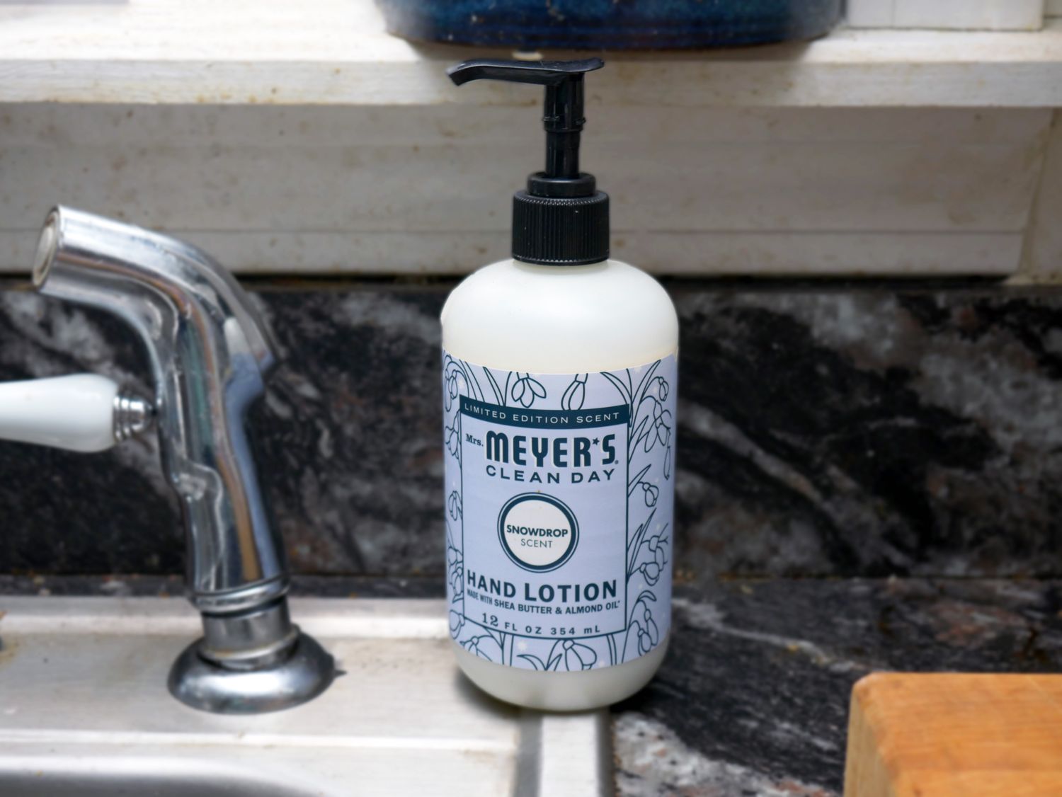 Mrs Meyers Clean Day hand lotion bottle on a kitchen counter next to a sink faucet