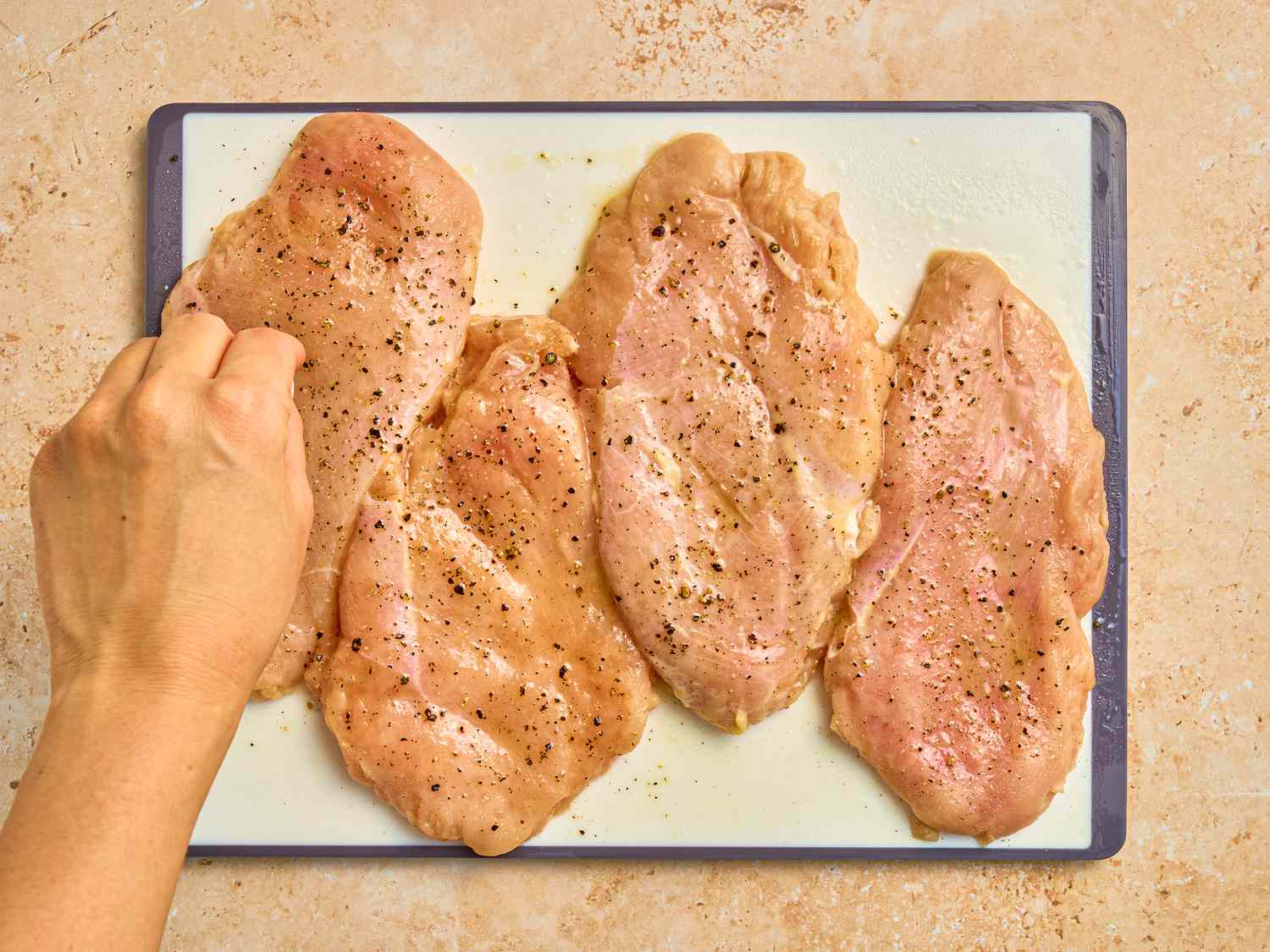 Seasoning raw chicken on a cutting board