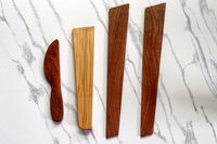 Four wooden utensils of differing shapes placed on a white and gray background including a knife and spatulalike items