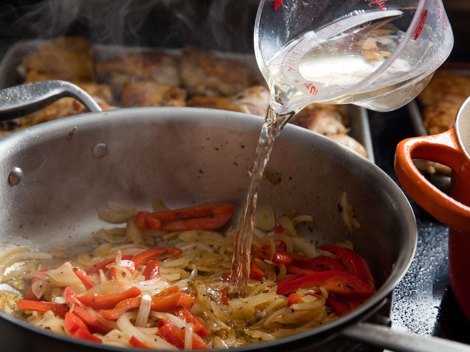 Adding wine to a saute pan of chicken cacciatore. 