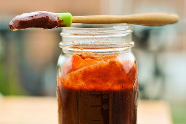 A mason jar filled with homemade cherry barbecue sauce, and a silicone pastry brush dipped in sauce is laying across the rim of the jar.