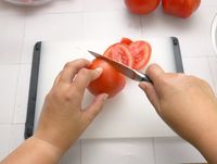 a person slicing a tomato into rounds with a paring knife