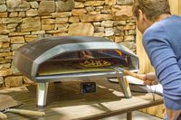 A person examines a pizza cooking in the Ooni Koda 2 Max Gas Powered Pizza Oven